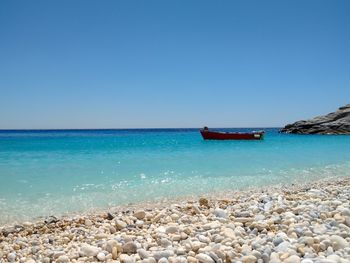 Boat moored on sea against clear blue sky