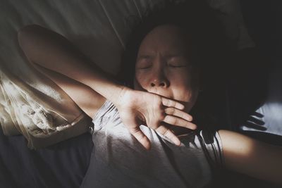 High angle view of woman yawning while lying on bed at home