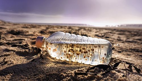 Close-up of water bottle on beach against sky
