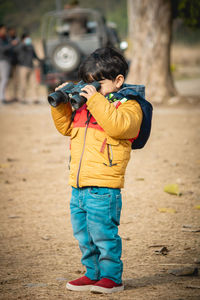 Side view of a boy standing on the road with binoculars
