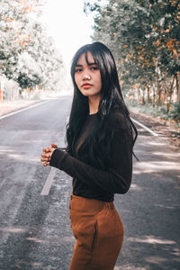 Young woman standing on road against trees