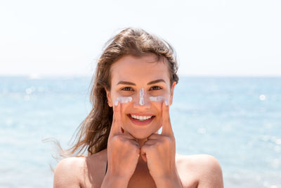 Portrait of smiling woman applying suntan lotion at beach against sky