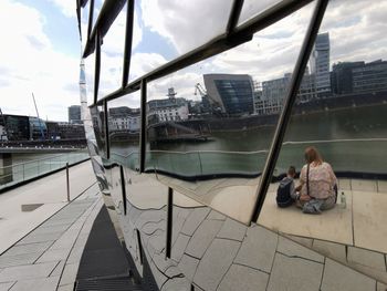 Man sitting in city against sky