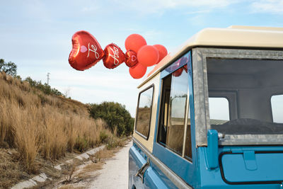 Low angle of vintage shiny car with red air balloons in shape of heart parked on sandy road in countryside