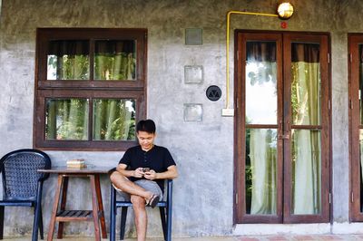 Man using phone while sitting on chair outside house