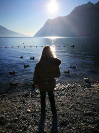 Rear view of girls standing at lakeshore during sunset