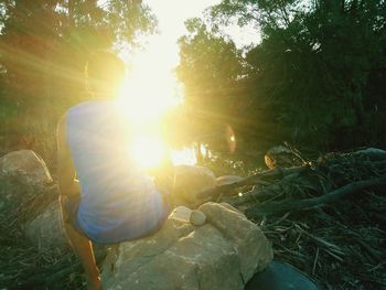 Man sitting on land in forest against bright sun
