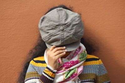 Woman covering face with cap while against brick wall