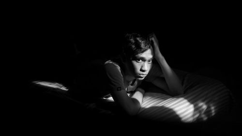 High angle portrait of young man lying on bed in darkroom