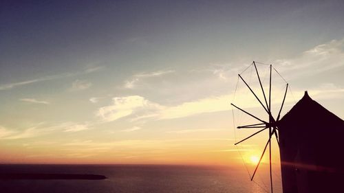 Silhouette of traditional windmill by sea against sky