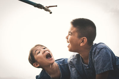 Close-up of playful siblings drinking water falling from faucet against clear sky