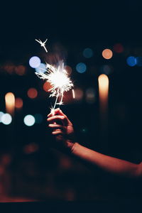 Cropped hand of person holding illuminated sparkler at night