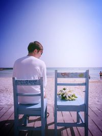 Rear view of man on bench by sea against clear sky