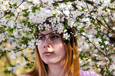 Portrait of beautiful young woman against white flowering tree