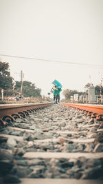 Rear view of people walking on railroad track against sky