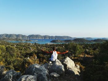 Rear view of man sitting on rock against sky