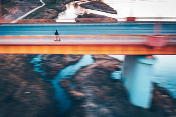 Blurred motion of person riding push scooter on bridge