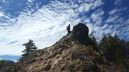 Low angle view of hiker standing on mountain against cloudy sky