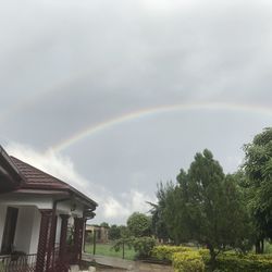 Scenic view of rainbow over house and trees against sky
