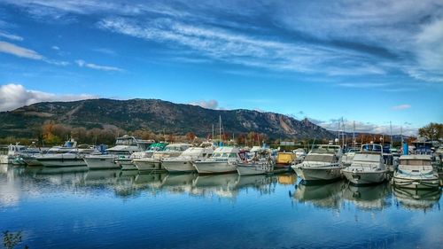 Boats in calm sea against cloudy sky