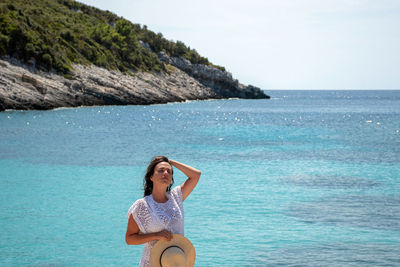 Front view of attractive young woman wearing beach clothes, standing on sea shore