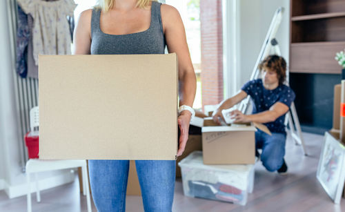 Midsection of woman holding cardboard box with man in background