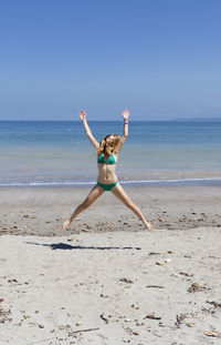 Woman in bikini jumping at shore against clear sky