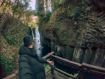 Portrait of young man standing by railing in forest