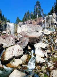 View of rocks and trees against clear blue sky