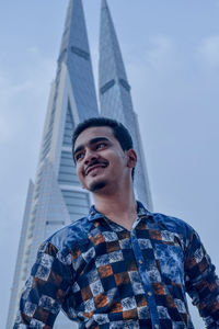 Low angle view of smiling young man standing against modern building in city