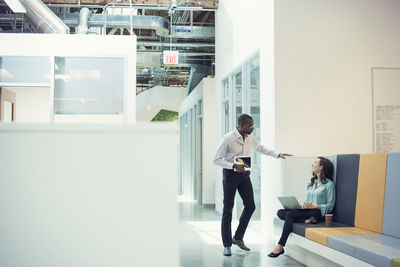 Colleagues talking in corridor, using mobile devices