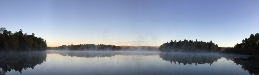 Reflection of trees in calm lake against clear sky