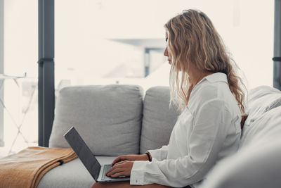 Young woman using laptop while sitting on bed at home