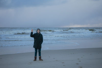 Cold stormy winter sea, a small man stands in full growth with his hand raised with two fingers