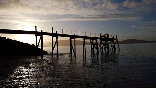 Silhouette bridge over sea against sky during sunset
