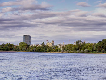 View of buildings by river against cloudy sky