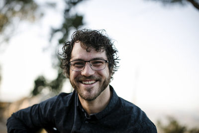 Close-up portrait of happy handsome man sitting against clear sky at park