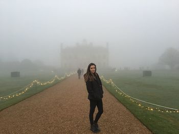 Portrait of woman standing on walkway against kingston lacy during foggy weather