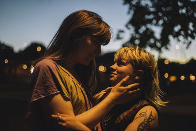 Young transgender woman looking at non-binary person at night