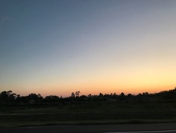 Silhouette trees on field against clear sky