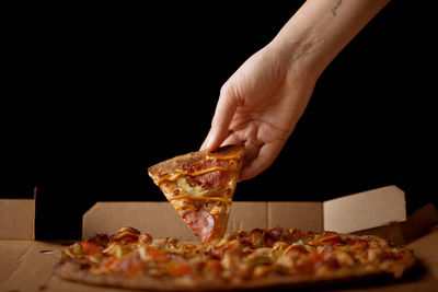 Close-up of hand holding pizza over black background