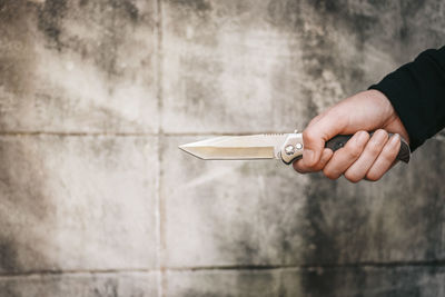 Cropped hand of burglar holding knife against wall