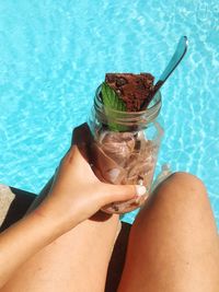 Low section of woman holding jar with dessert at poolside on sunny day