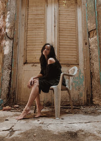 Portrait of young woman sitting on old abandoned house