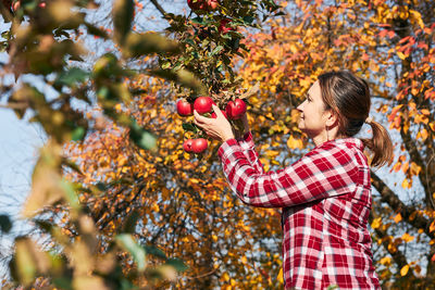 Side view of young woman standing by tree