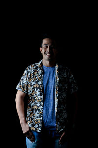 Portrait of young man standing against black background