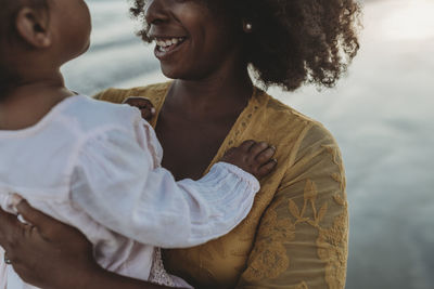 Close up detail of daughters hands embracing mother at beach