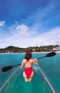 Rear view of woman kayaking in sea against sky