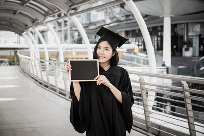 Portrait of woman wearing graduation gown while standing on bridge