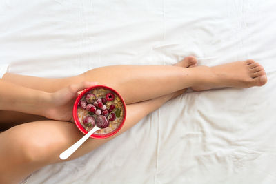 Low section of woman with breakfast in bowl on bed at home